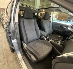 Front interior of a car with black cloth seats and sunroof, driver's door open in a showroom.