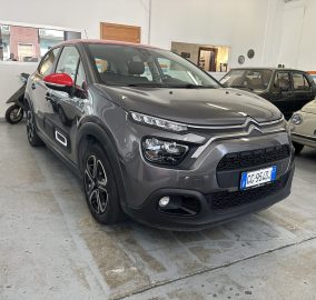 Gray SUV in a car showroom with red side mirrors and chrome grille, other classic cars visible in background