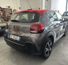 Rear view of a gray Citroën C3 parked in a garage or showroom, with other cars and shelves in the background.