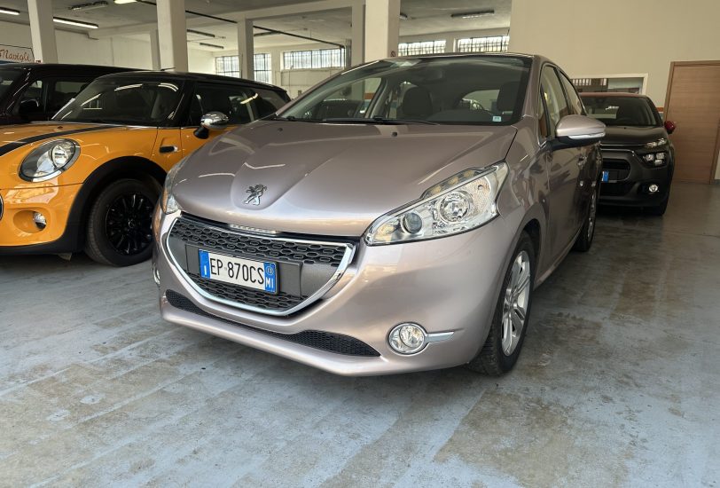Interior of a car showroom/garage with a silver Peugeot in the foreground and an orange Mini to its left. Other vehicles visible in the background.