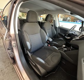 Interior view of a car showing front seats, steering wheel, and dashboard with the door open at a dealership or showroom.