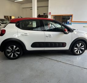 White compact SUV with a red roof parked inside a garage; another vehicle is visible in the background.