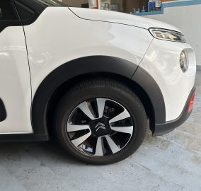 Close-up of a white SUV's front left area, showing the headlight, wheel, and fender with black trim.