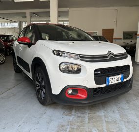 Front view of a white SUV with red accents parked inside a car showroom/garage