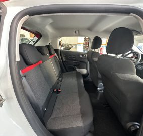 Rear passenger seats in a compact car, black fabric with red stitching, open side door showing the cabin