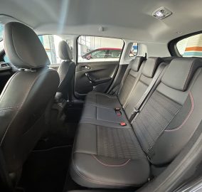 Rear passenger seats in a black leather interior with red contrast stitching and headrests, shown from a wide-angle inside a car.