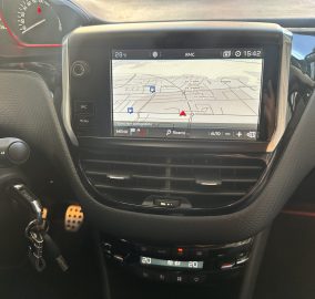 Car dashboard center console displaying a GPS navigation map on a touchscreen, with street names and a red vehicle icon.