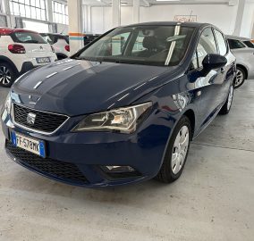 Front three-quarter view of a dark blue car in a bright indoor dealership with other cars parked nearby (license plate FF-578MK).
