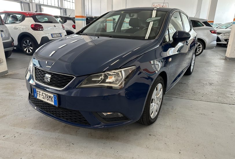 Front three-quarter view of a dark blue car in a bright indoor dealership with other cars parked nearby (license plate FF-578MK).