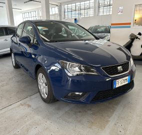 Blue hatchback car parked in an indoor parking garage with a silver car to the left and a motorcycle to the right.