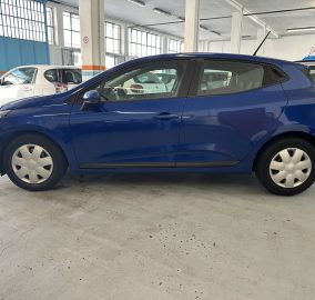Blue compact hatchback parked inside a well-lit garage with other cars in the background and blue walls outside windows.