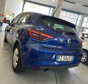 Blue Renault Clio rear view parked in a garage, other car beside it, license plate visible (EU).