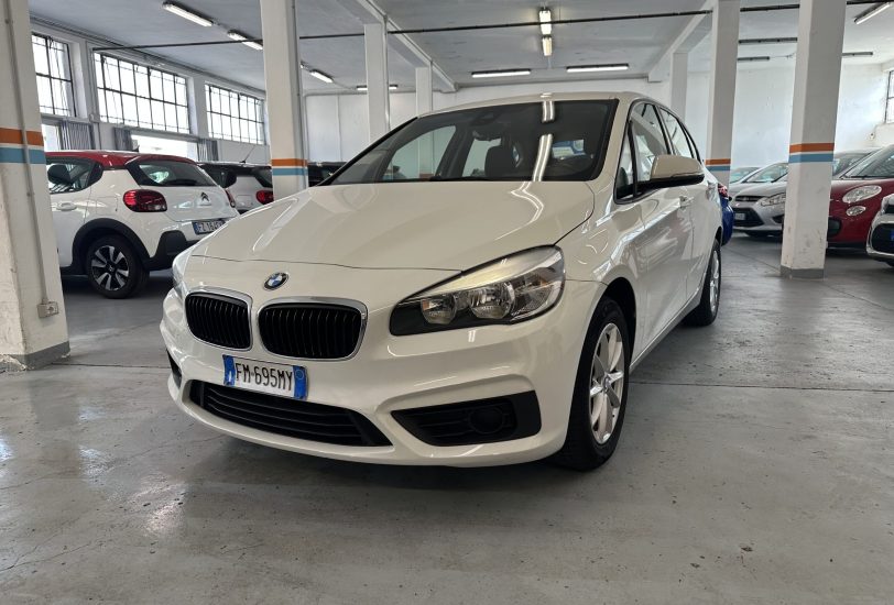 White BMW sedan in a dimly lit indoor parking garage with other cars and concrete pillars nearby.