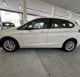 White BMW SUV parked indoors in a garage with another car in the background.