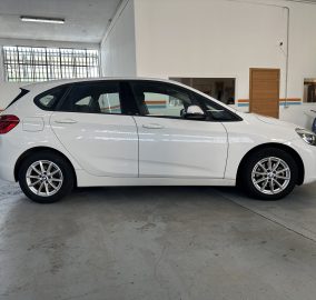 White BMW SUV parked indoors in a showroom with large windows and other cars nearby.