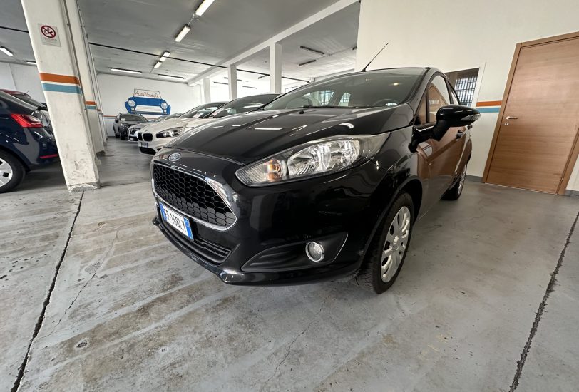 Black car parked in a dim indoor showroom with other cars lined up in the background and concrete floor.【Informative】