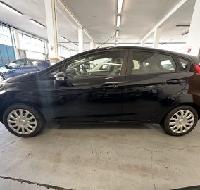 Black hatchback parked indoors in a garage with a blue car in the background and white support columns.