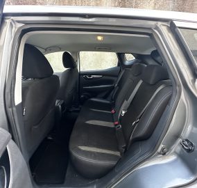 Interior of a car's rear passenger area with black fabric seats and headrests, viewed from the open rear door
