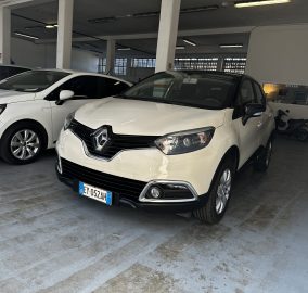 White Renault SUV parked in a showroom beside another white car, concrete floor and pillars visible in a bright indoor space