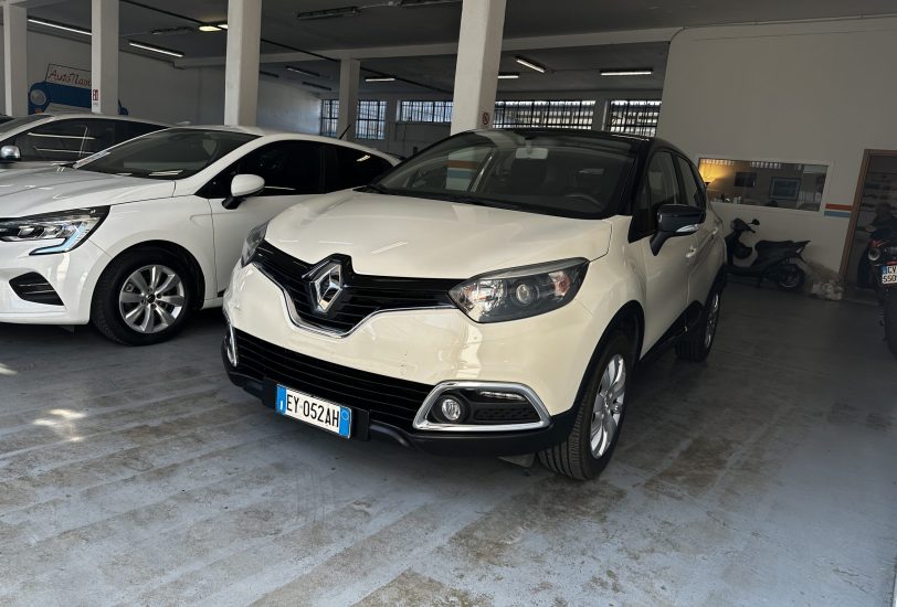 White Renault SUV parked in a showroom beside another white car, concrete floor and pillars visible in a bright indoor space