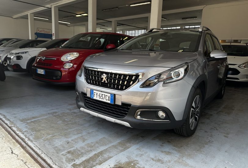 Silver Peugeot SUV in the foreground inside an indoor car showroom with other parked cars nearby.