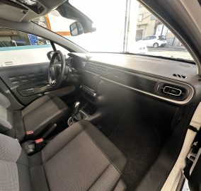 Front interior of a car showing the driver’s seat, steering wheel, center console, and dashboard from the passenger side window view.