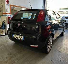 Black Fiat Punto parked in a garage with tools and a red fire extinguisher on the wall nearby; another car visible in the background.