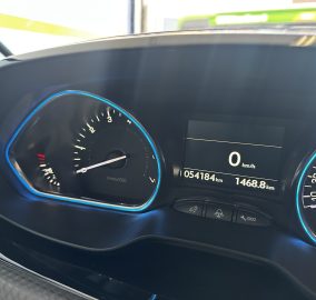Car dashboard with a digital speed readout showing 0 km/h, odometer 54,184 km, and trip 1,468.8 km visible between tachometer and speedometer rings.