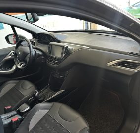 Interior of a modern car showing the driver's seat, steering wheel, center touchscreen, and front passenger area with black upholstery and metallic trim.