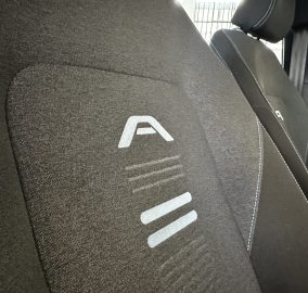 Close-up of a dark fabric car seat with white stitching and a partial white logo.