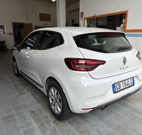 White Renault Clio parked in an indoor garage, rear three-quarter view showing taillights and license plate.
