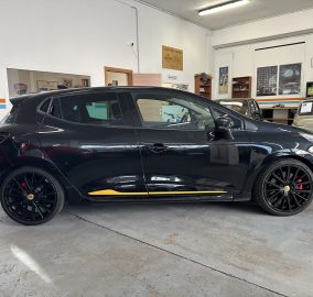 Black SUV parked indoors in a classic car showroom, with a beige vintage car in the background and retro posters on the wall.