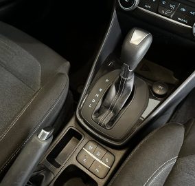 Center console featuring an automatic gear shift with climate control dials and control buttons nearby in a dark car interior