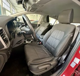 Interior of a red car showing the driver and front passenger seats, steering wheel, and dashboard from the open driver’s door.