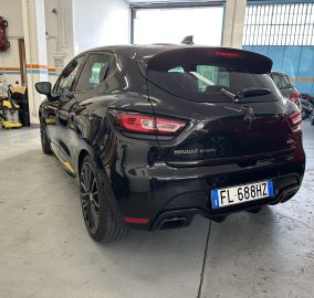 Rear view of a black Renault SUV inside a garage or workshop, showing red taillights and a European license plate (FL-688HZ). Other cars and workshop equipment are visible in the background.