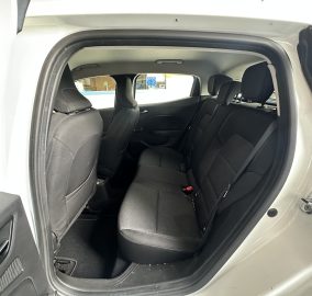 Rear passenger area of a car with the door open, showing black fabric seats and headrests inside a light-colored SUV/Cuv.