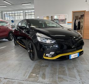 Front three-quarter view of a glossy black SUV with yellow bumper trim, parked beside a red SUV inside a showroom/garage.