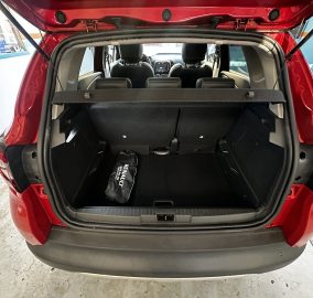 Open trunk of a red SUV showing the cargo area with rear seats upright and a Renault-branded bag in the floor space